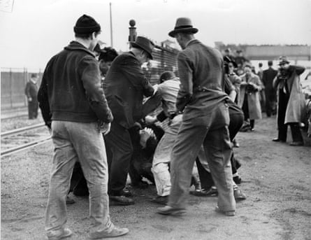 Men wearing hats are seen from behind next to what appears to be a pile of people wrestling with each other