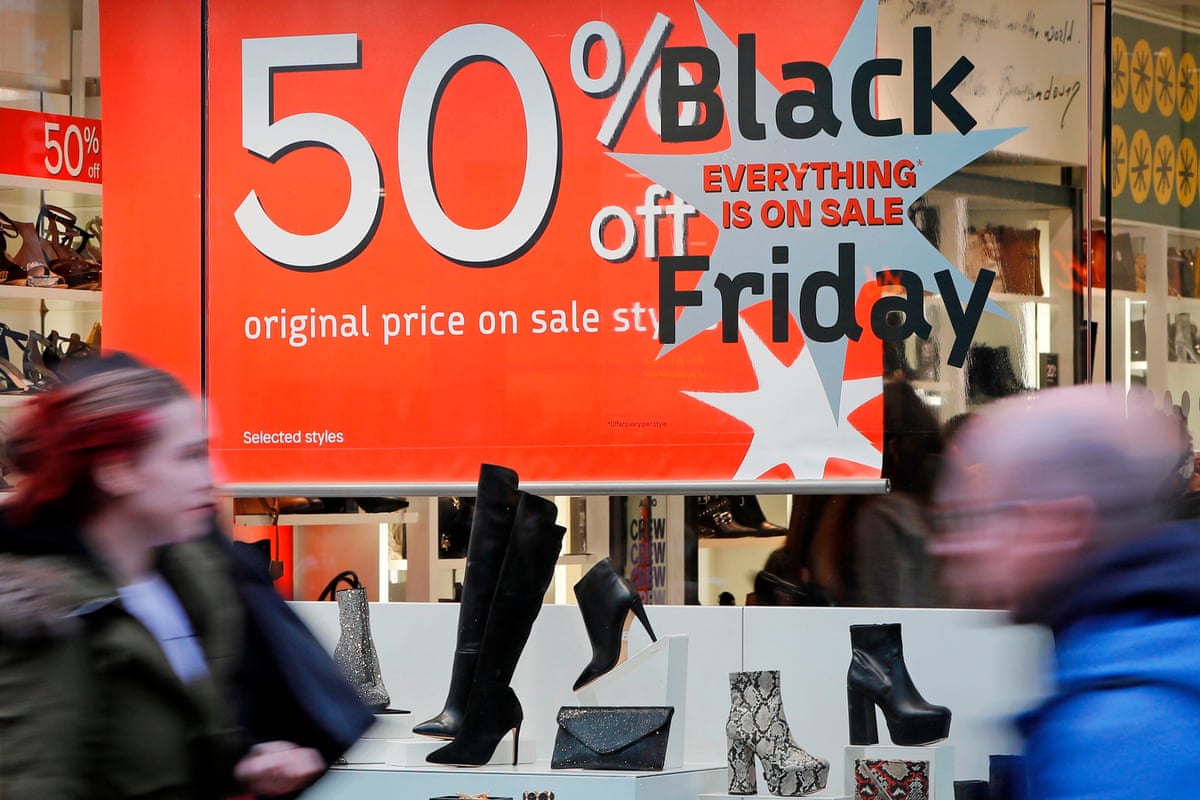 Shoppers pass a promotional sign for ‘Black Friday’ sales discounts