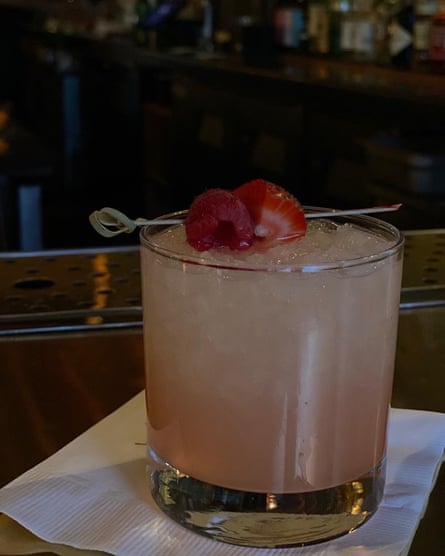 An image of a pink cocktail topped off with a raspberry and strawberry on a toothpick.