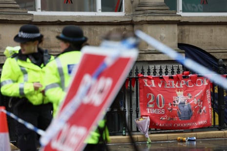 Police officers operate as a Liverpool FC flag is seen in the background at the site of the incident where a car plowed into a crowd of Liverpool fans during a parade.