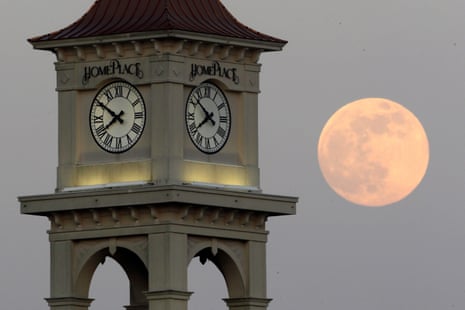 Gorgeous full pink moon in sky beyond a clock tower.