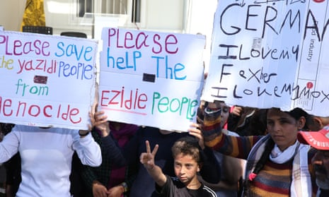 Migrants hold signs reading “Please help Yazidi people” as they wait for Pope Francis on the Greek island of Lesbos.