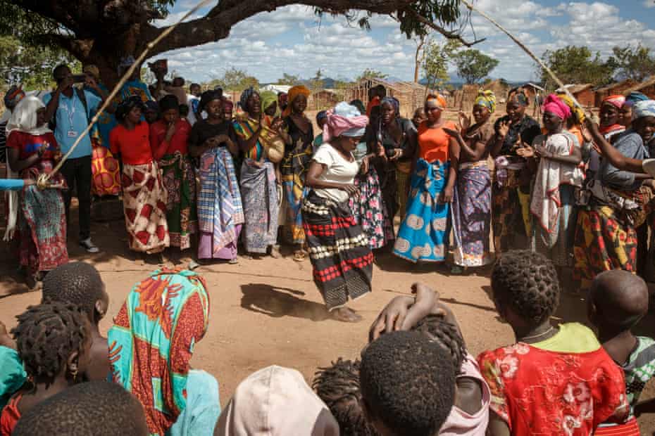 Woman skipping on a big rope in circle of of women clapping hands.