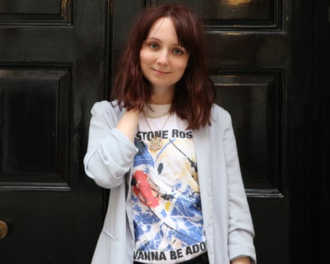 close up of Claire Eastham wearing white jacket and white Stone Roses T-shirt with shoulder length brown hair in front of a black front door
