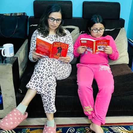 A woman and a girl sit on a sofa in night clothes reading books