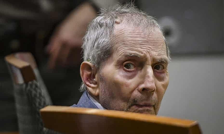 A closeup shot of an elderly man turned around in his chair in a courtroom.