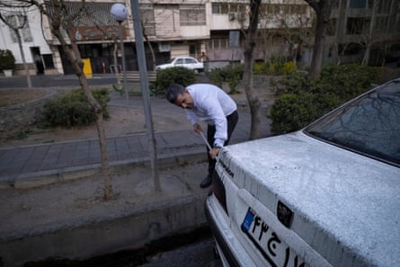 An Iranian man cleans a white car covered with oil-soot residue/