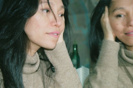 A woman wearing a beige turtleneck sweater holds her head in her hand