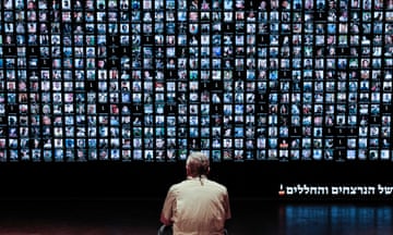 A man sits in front of a digital screen displaying the portraits of more than 1,500 people