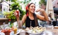 Alex Karol eats oysters, holding a bottle of hot sauce, at an outdoor restaurant table