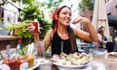 Alex Karol eats oysters, holding a bottle of hot sauce, at an outdoor restaurant table