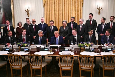 Donald Trump speaks while seated at a table between tech executives and a line of people standing behind him