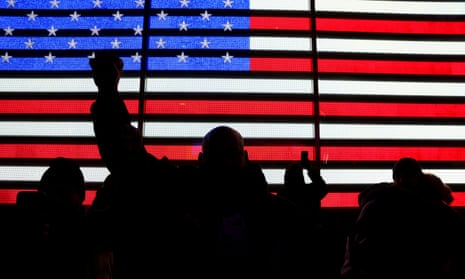 Protestors in New York’s Times Square. Silhouettes of protestors against a screen showing an American flag. One protestor’s fist is raised. 