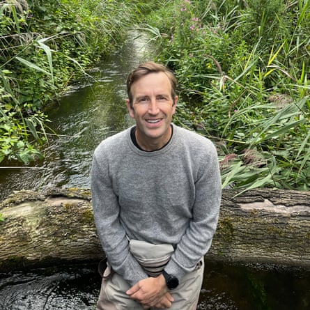 Writer Robert Macfarlane sits on a log in the middle of a stream
