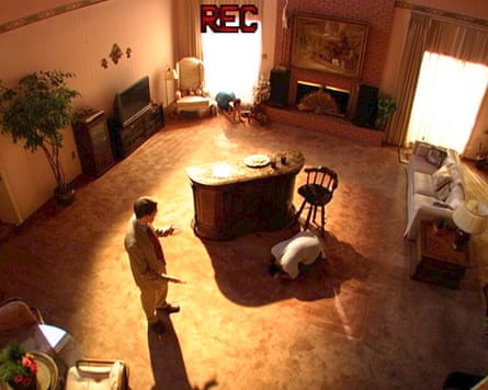 Aerial view of a man in a living room kneeling on the floor and another man in a suit talking to him.