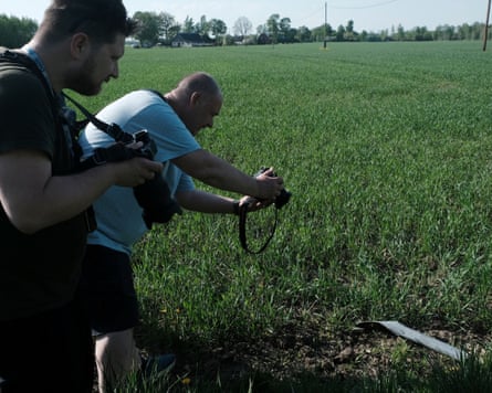 Two men take photographs of a piece of metal in a field