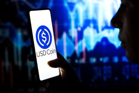 A photo illustration shows a person holding a smartphone that is displaying the logo for USD Coin.
