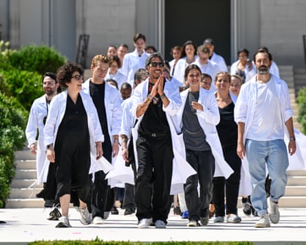 Pierpaolo Piccioli wearing a white doctor’s coat surrounded by others in the same coat claps as he walks down the catwalk after his show at Cité Universitaire de Paris.