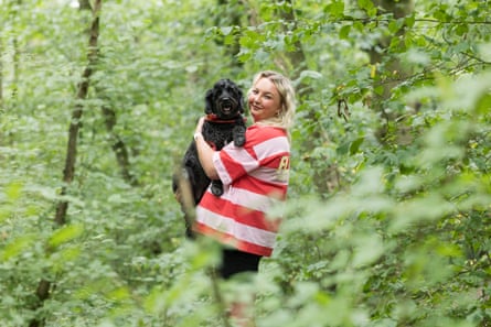 A woman cuddling a black dog, surrounded by trees and leaves.