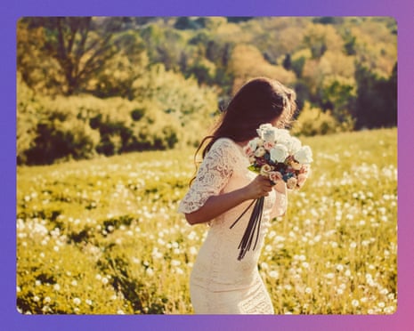 A bride in a white lace dress holds a bouquet in a sunny wildflower meadow