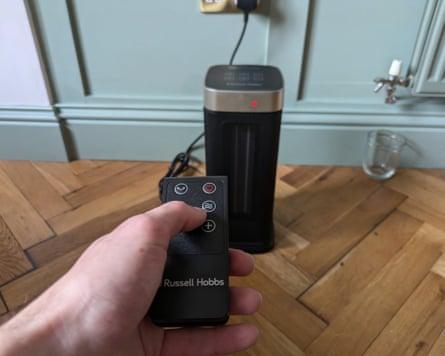 A person controls a black electric heater with its remote control