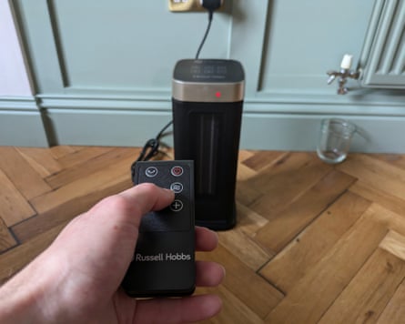 A person controls a black electric heater with its remote control
