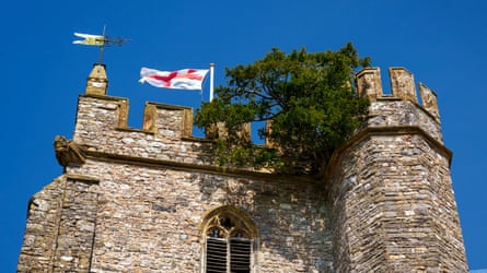 A yew tree growing at the top of a church tower with an English flag flying next to it