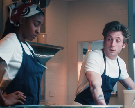 Jeremy Allen White and Ayo Edebiri wearing white T-shirts and blue aprons.
