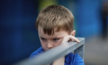 Small boy in school uniform holding a railing and looking sad