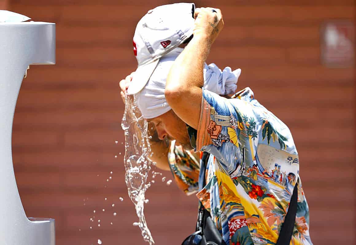Buddy Willer, wearing a colorful shirt and a white head covering, splashes water upon himself at a water refilling station in Las Vegas.