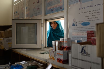 An Afghan woman in a hijab looks through a small window that acts as a pharmacy serving hatch