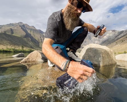 man crouching on rock fills up water bottle from creek outside