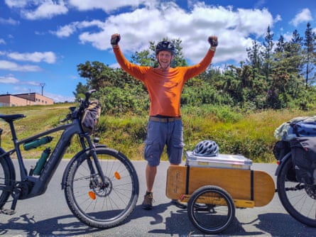 Cyclist in orange jersey with arms aloft celebrating with ebike after a steep climb.