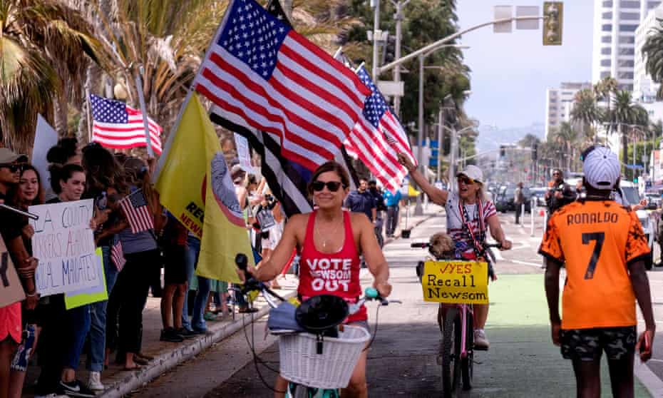 Cyclists with signs in support of the recall effort ride past anti-vaccination protesters taking part in a rally against Covid-19 vaccine mandates, in Santa Monica, California.