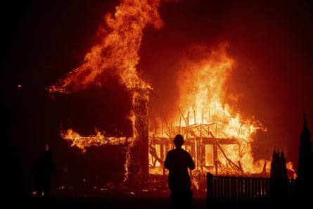 a firefighter looks as flames engulf a house