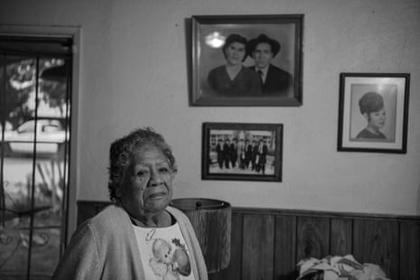 An older woman stands in front of hanging family photos