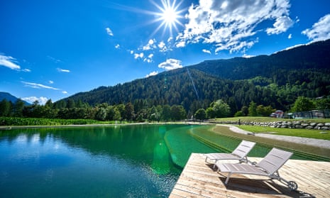 A clear, turqouise-green swimming lake with the mountains in the background and a blue sky.