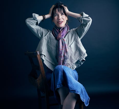 Sally Hawkins sitting on a chair with her legs crossed and her hands in her hair. She is wearing a loose grey top, a blue denim skirt and a scarf. From The Shape of Water.