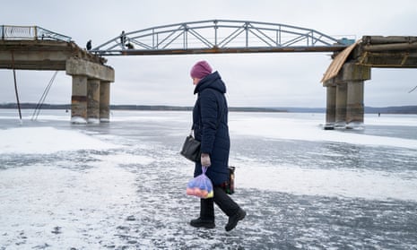 A woman walks across the frozen Siverskyi Donets River as workers repair a bombed bridge in Staryi Saltiv.