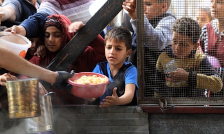 A child among a group of children reaches out to take a bowl of food