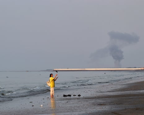 A woman at the water's edge on the strait of Hormuz off Bandar Abbas, Iran, as smoke rises in the background after an explosion on Monday