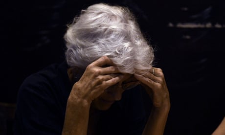 An older white person with white hair looks down, holding their head with both hands. during a presidential debate