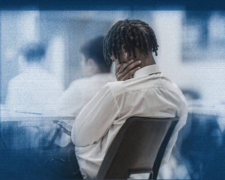 A boy leaning back in his chair looking at his phone at school