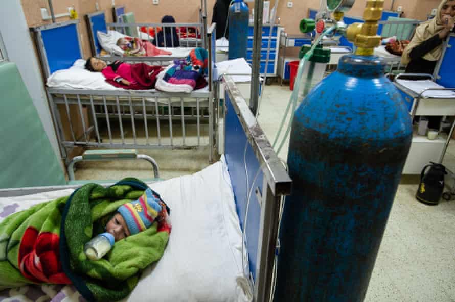 طفل رضيع ملفوف في بطانية يرقد على سرير في جناح المستشفى ويمص زجاجة الحليب مع أطفال صغار آخرين على أسرة أخرى 