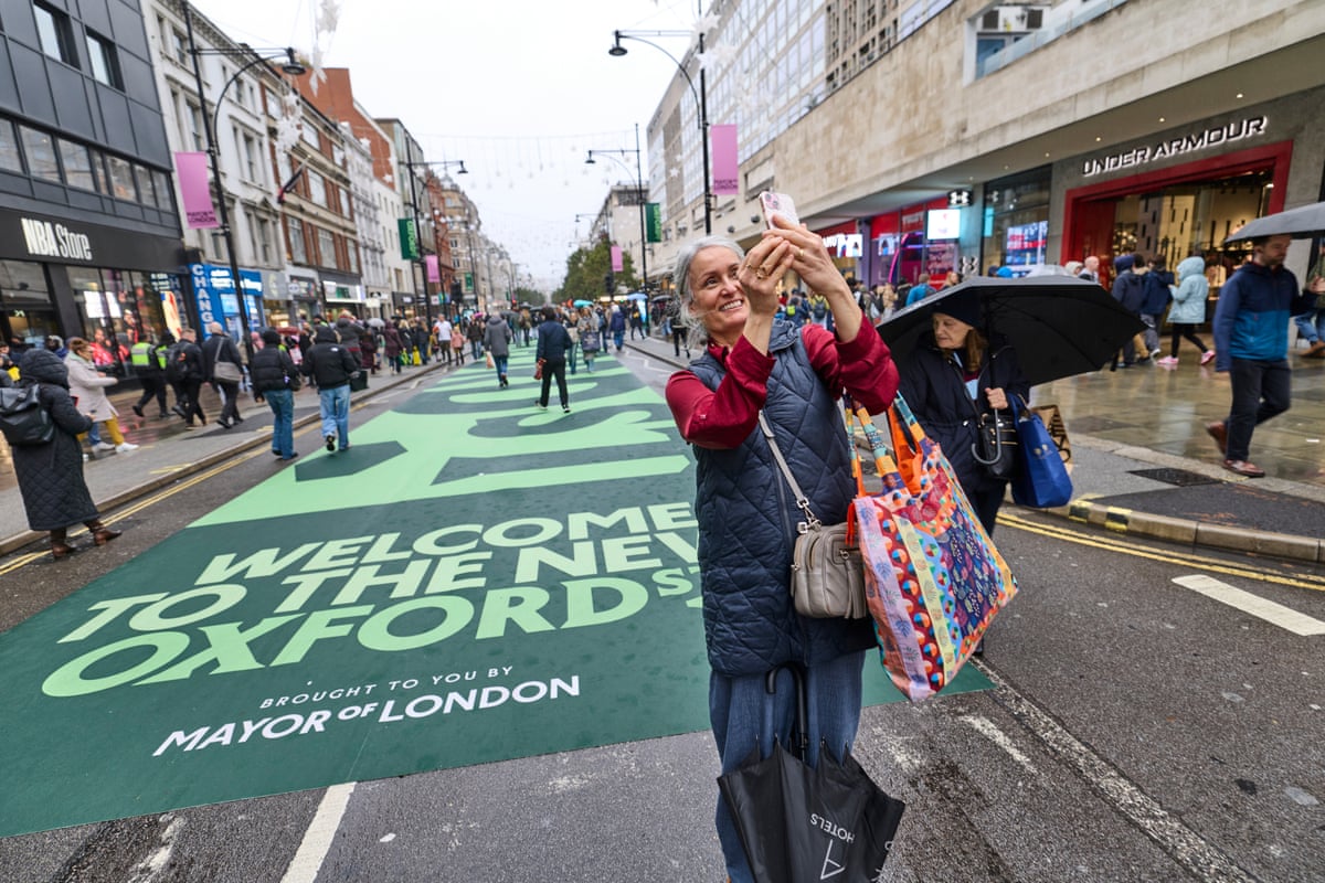 Raquel Cox stands in the street holding up her phone. She carries a colourful shopping bag.