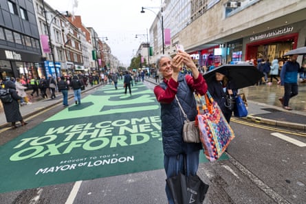 Raquel Cox stands in the street holding up her phone. She carries a colourful shopping bag.