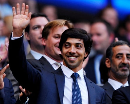 Sheikh Mansour bin Zayed al-Nahyan, wearing a suit and tie, waving to fans inside the Etihad Stadium.