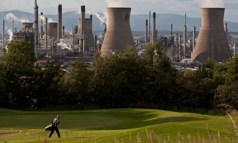 A golfer walks along a fairway in front of a backdrop of the pipes, equipment and cooling towers of the Grangemouth refinery