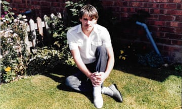 A young man poses for a photograph in a garden