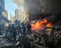 First responders in Beirut stand next to a razed building with a fire burning strongly beside them